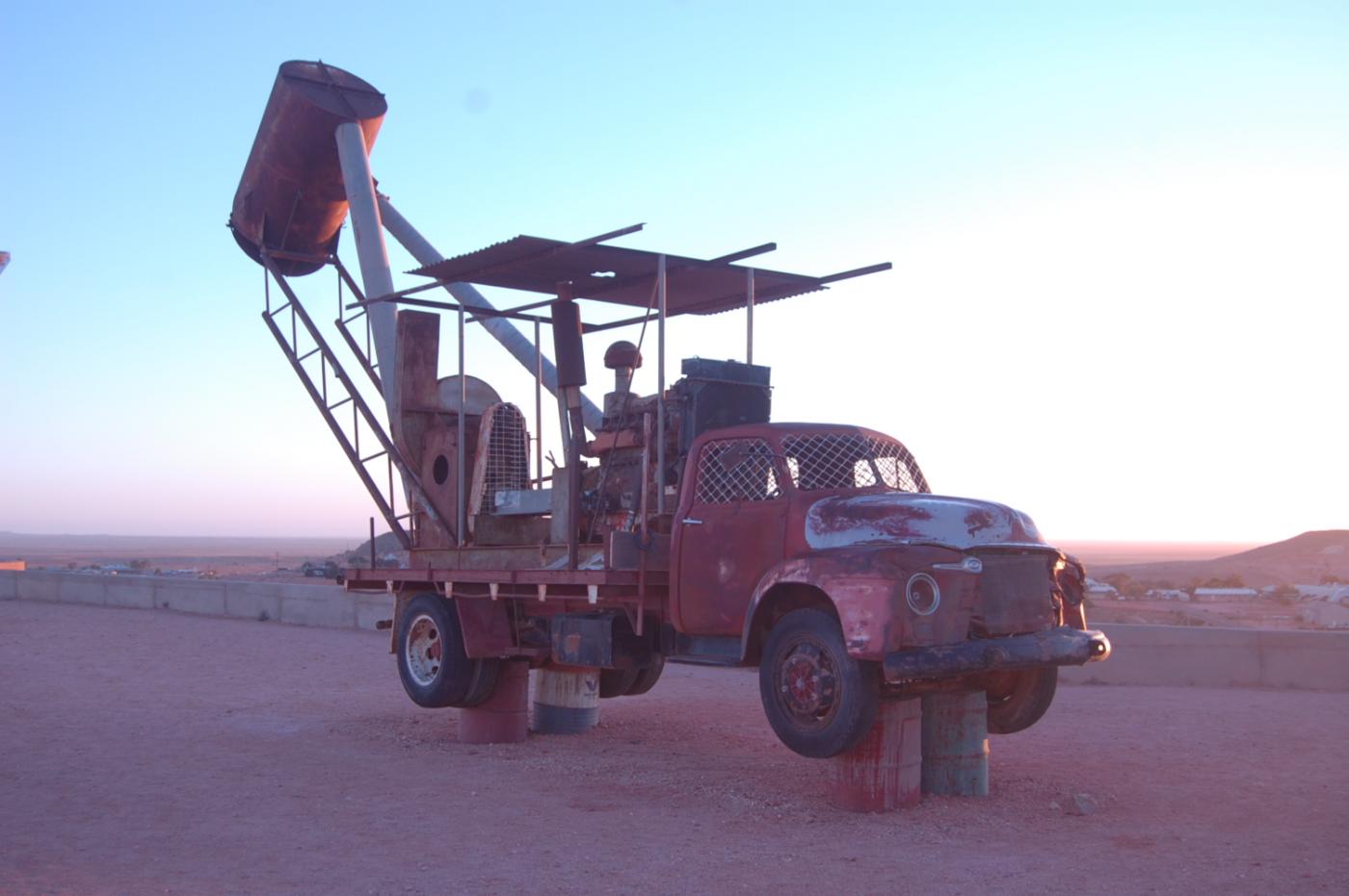 One of Coober Pedy&#039;s iconic mining vehicle is lit by the light of the rising desert sun.